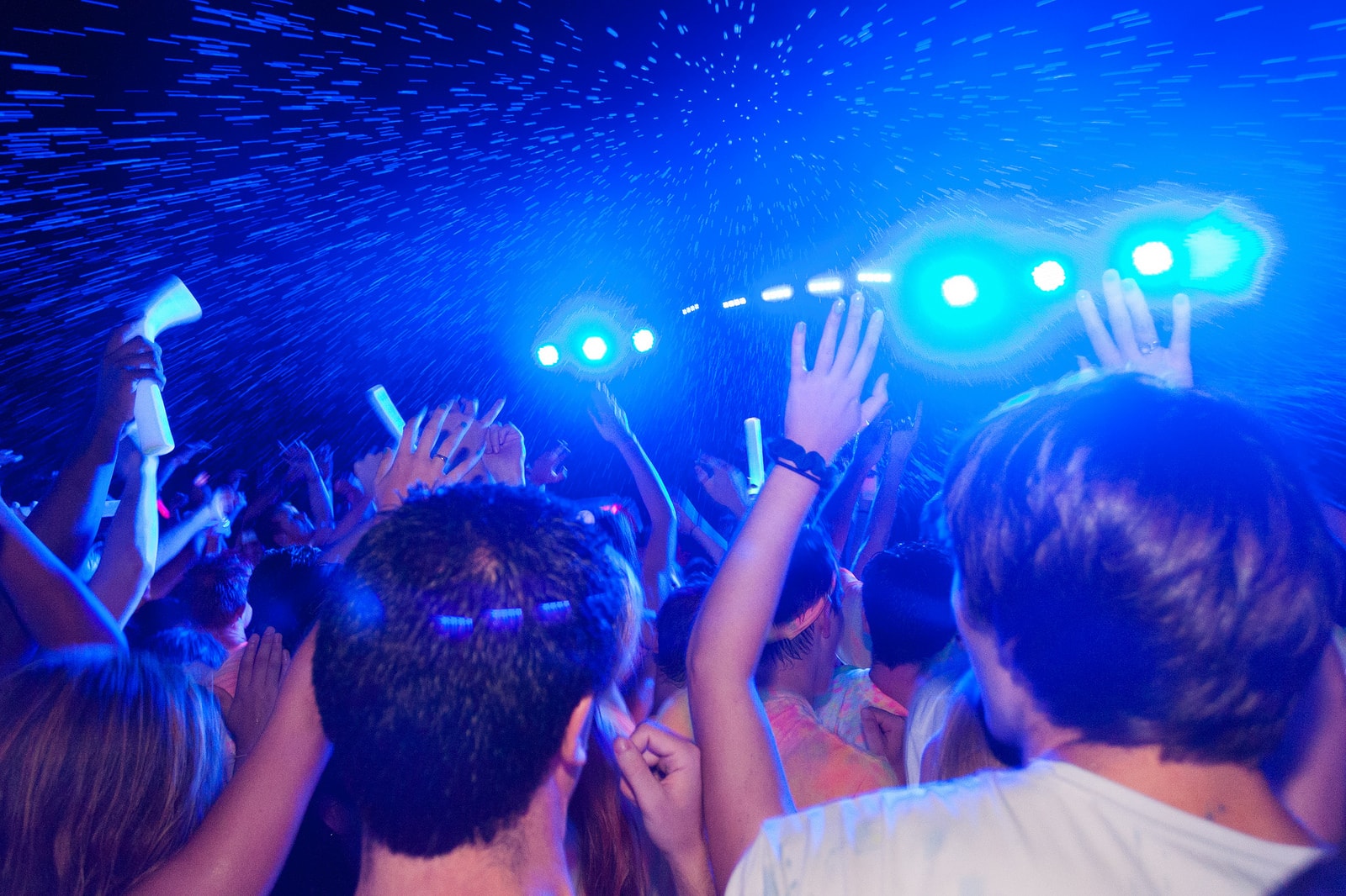 Crowd with hands raised under blue stage lighting and confetti at a GloZone DJ event