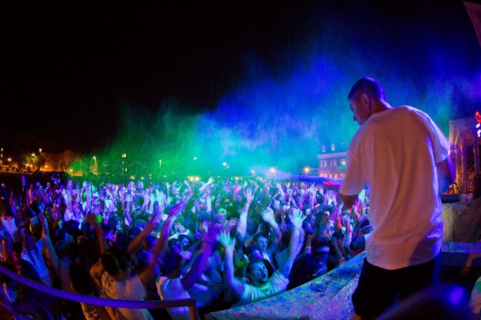 Wide shot of a massive crowd with hands raised under blue and green stage lighting at a GloZone event