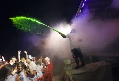 DJ spraying green glow powder over an energetic crowd at a nighttime GloZone event