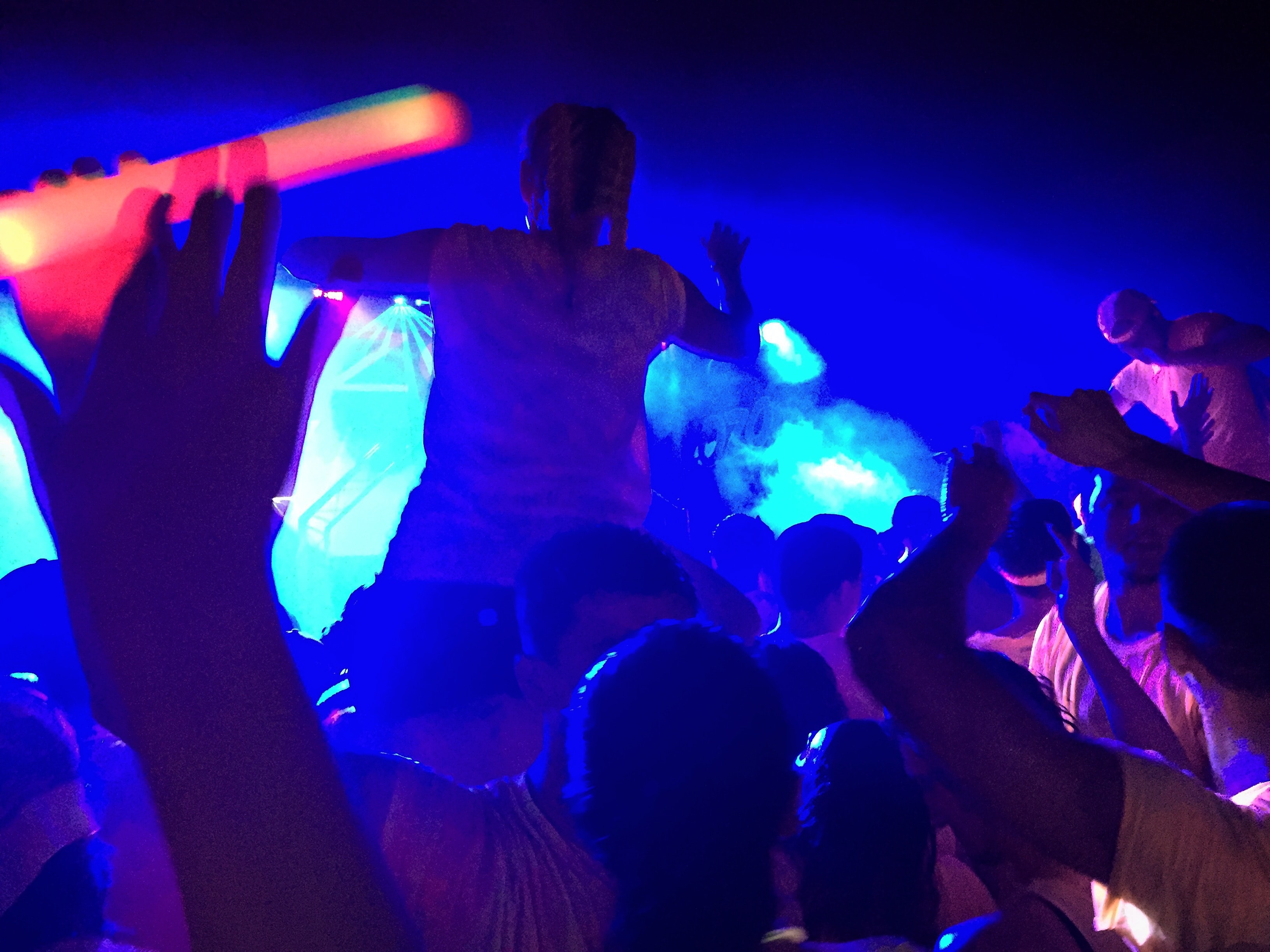 DJ performing on stage with crowd hands raised under blue and teal lighting at GloZone HTown 2016